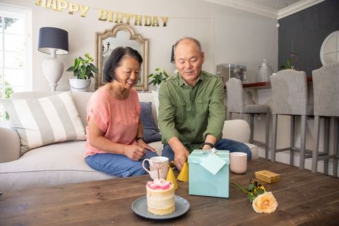 Senior asian couple celebrating birthday at home opening teal gift box