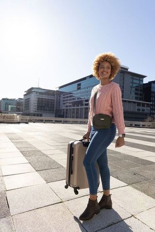 African american woman traveling in modern city plaza pulling luggage in sunlight