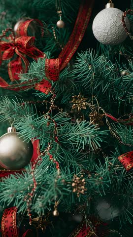Vertical video panning down fir tree revealing baubles and red ribbon festive close-up