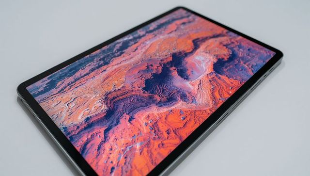Slim tablet displaying vibrant abstract topographic wallpaper on white surface, tilted