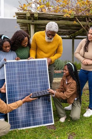 Family installing solar panel in backyard hands-on intergenerational african american teamwork