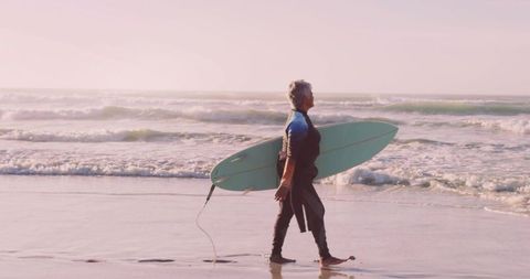 Senior Woman Walking with Surfboard on Beach During Sunrise