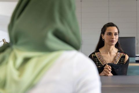 Two female colleagues sitting across desk having calm meeting wearing hijab and embroidered top