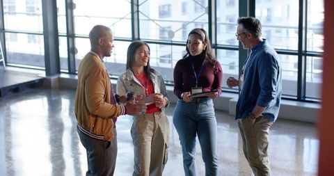 Diverse team networking in modern glass atrium sharing ideas with tablet and coffee