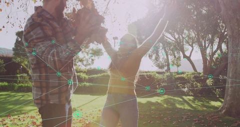 Backlit couple celebrating in park with sunflare, falling leaves and digital network overlay