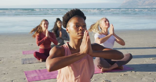 A diverse group of women meditating on a sandy beach during sunrise. They are sitting on yoga mats and holding a prayer position, focusing on mindfulness and peace. Perfect for wellness blogs, meditation retreats, eco-tourism promotions, and motivational content about fitness and healthy living.