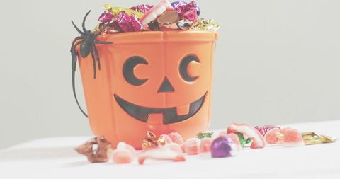 Jack-o-lantern candy bucket overflowing with foil-wrapped chocolates and gummy treats for halloween