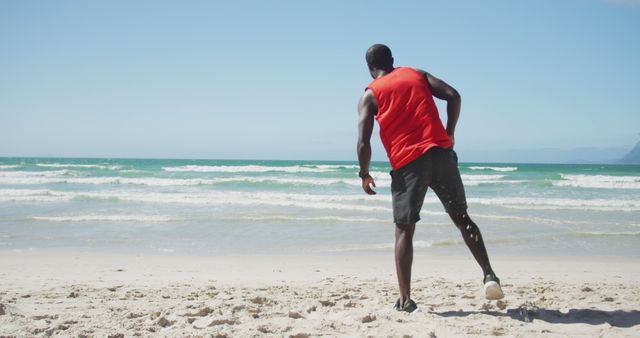 African american man stretching on the beach, exercising outdoors by the sea. fitness, healthy and active lifestyle concept.