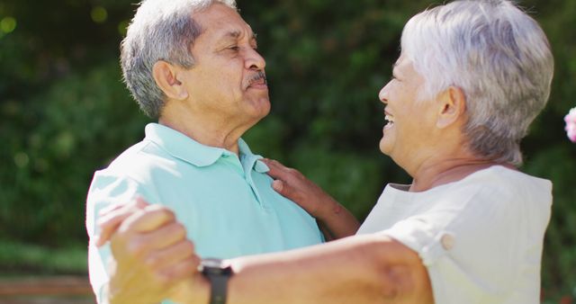 Image of happy biracial senior couple holding hands and dancing in garden. active retirement lifestyle, senior relationship and spending time together concept.