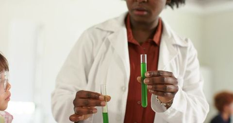 African american science teacher demonstrating green test tube experiment to asian student