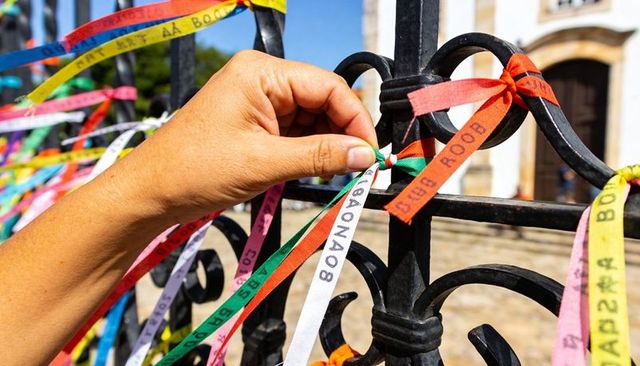 Right hand tying colorful wish ribbons to wrought-iron fence at historic church plaza