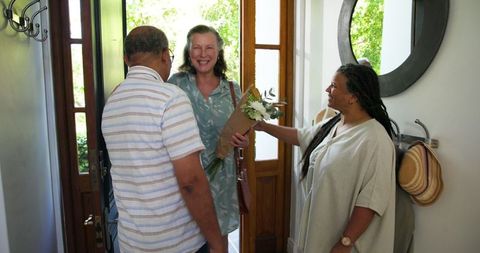 Joyful Senior Couple Welcoming Friends with Flowers at Door
