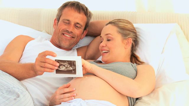 Expectant parents relaxing together and smiling while viewing an ultrasound scan of their unborn baby. Useful for content related to family bonding, antepartum milestones, and parenthood narratives.