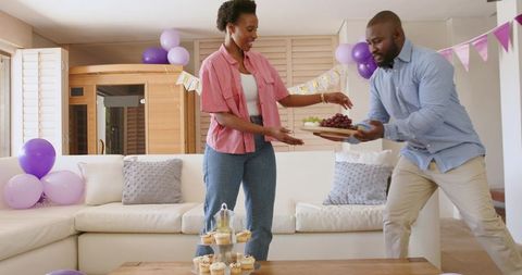 African american couple arranging desserts and passing platter for home party celebration
