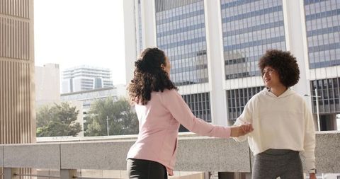 African American friends holding hands on urban terrace near modern office towers