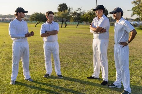Cricket teammates discussing strategy on sunlit field in classic white uniforms