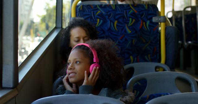 African american girl sitting in city bus using headphones. Communication, childhood, transport, city living and lifestyle, unaltered.