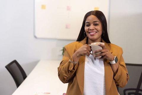 African american professional woman smiling and holding coffee mug in modern meeting room