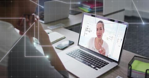 Remote video call on laptop showing woman presenting while colleague focusing at office desk
