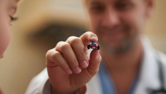 Pediatrician holding tiny toy car comforting child during clinic exam
