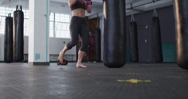 Caucasian female boxer wearing boxing gloves kicking the punching bag at the gym. sports, training and fitness concept