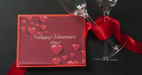 Valentine's Day greeting card with champagne flutes and red satin ribbon on dark backdrop