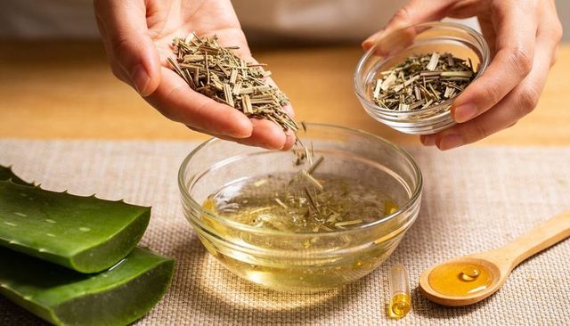 Hands pouring dried herbs into aloe infusion for natural skincare and diy remedies