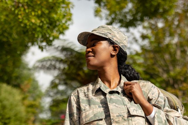 This image depicts a confident African American female soldier in uniform, looking away while outdoors. Ideal for use in articles, advertisements, or campaigns related to military service, patriotism, women's empowerment, and diversity in the armed forces.
