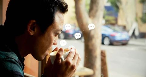 Sipping coffee, gazing through cafe window with chat bubble stickers, contemplative urban portrait