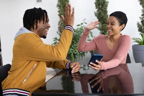 African american couple high-fiving over smartphone in bright outdoor courtyard