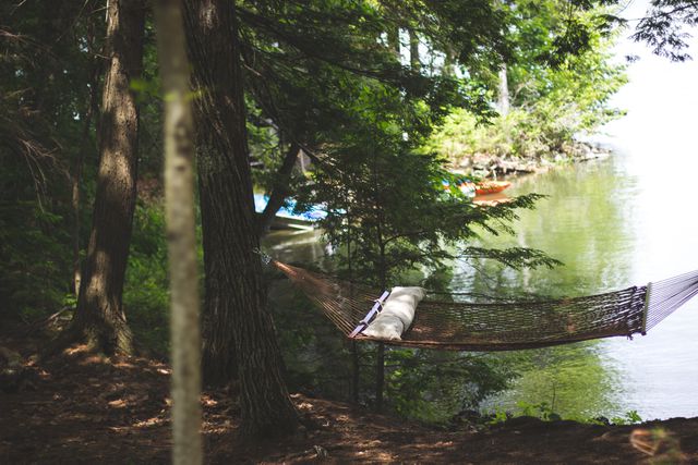 Hammock hanging between trees by serene lake, creating a tranquil and relaxing scene perfect for summer retreats and nature escapes. Ideal for travel commercials, blogs about outdoor recreation, or lifestyle articles focused on relaxation and peace.