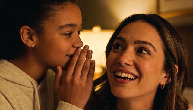 Child whispering secret to smiling mother by bedside lamp creating warm family bond