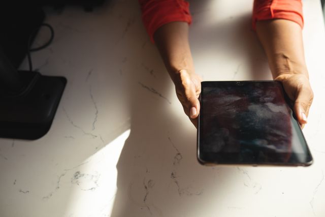 Hands holding a digital tablet on a marble table in a cafe. Ideal for use in articles or advertisements related to technology, small businesses, cafes, modern workspaces, and wireless devices. Can also be used for illustrating concepts of digital entrepreneurship and remote work.