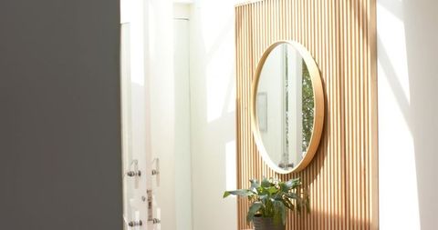 Sunlit modern entryway featuring round mirror, vertical wood slats and potted plant