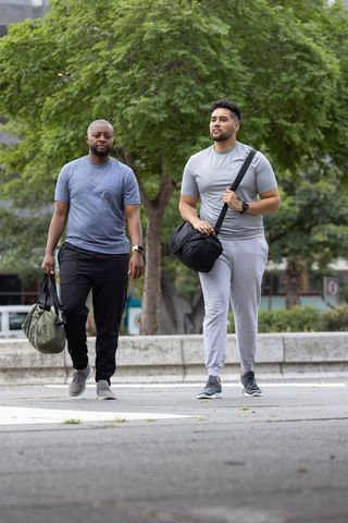 Two men walking together with duffel bags on urban plaza wearing casual fitness gear