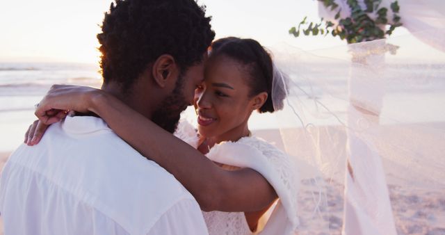 African american couple in love getting married, smiling and looking at other on the beach at sunset. marriage, love and romance, holiday by the sea.