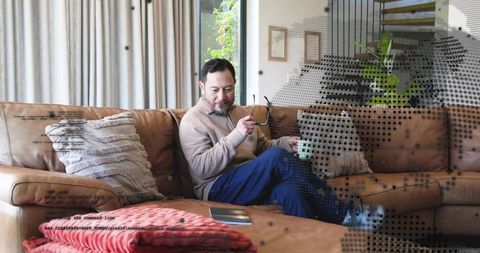 Relaxing asian man holding glasses and mug on leather sofa in cozy modern living room