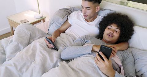 Father and Son Relaxing in Bed with Gadgets for Family Bonding