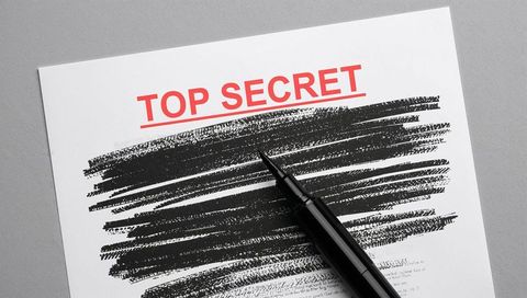 Top secret document with heavy black redaction lines, fountain pen resting on gray surface