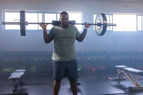 Backlit african american man lifting loaded barbell for strength training motivation
