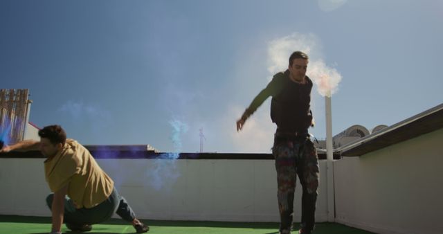 Two young men dancing energetically on a rooftop, backdropped by the blue sky. They are using dynamic movements with colorful smoke effects in the background, enhancing the vibrant and artistic feel of urban culture. This image can be used for promoting dance events, urban lifestyle blogs, performer portfolios, or energetic creative campaigns.