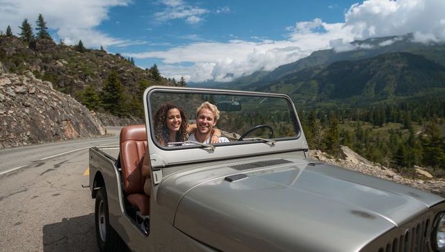 Couple enjoying scenic mountain drive in vintage open-top Jeep convertible