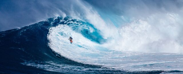 Person surfing large wave in ocean, showcasing extreme water sports and adventure. Ideal for use in sports, adventure, and lifestyle content highlighting surfing and ocean activities.