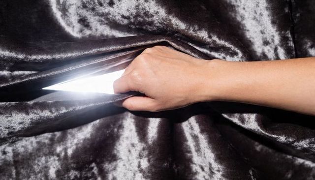 Closeup hand pulling dark velvet drapery revealing bright backlight through silky fabric