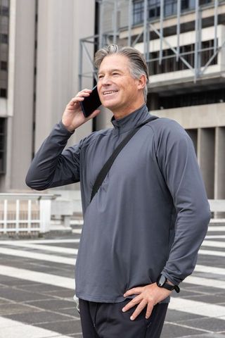 Mature man talking on phone on rooftop terrace wearing smartwatch and crossbody bag