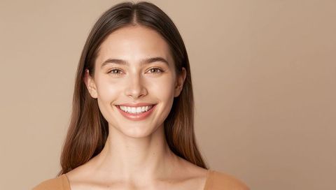 Smiling young woman with natural makeup and brown hair, minimalist beige portrait headshot