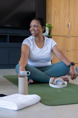 Senior african american woman stretching on yoga mat reaching water bottle smiling