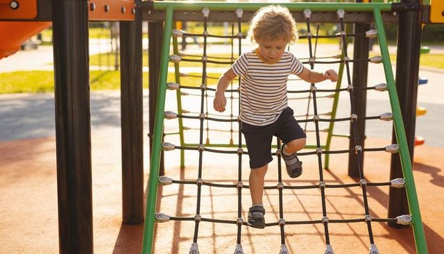 Young boy climbing rope net on sunny playground
