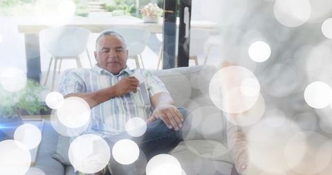 Relaxing calm senior man on sofa holding remote in bright modern living room with daylight