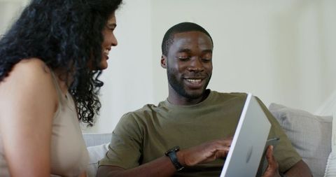 Couple sharing laptop on couch discussing business graphs and tech in cozy living room
